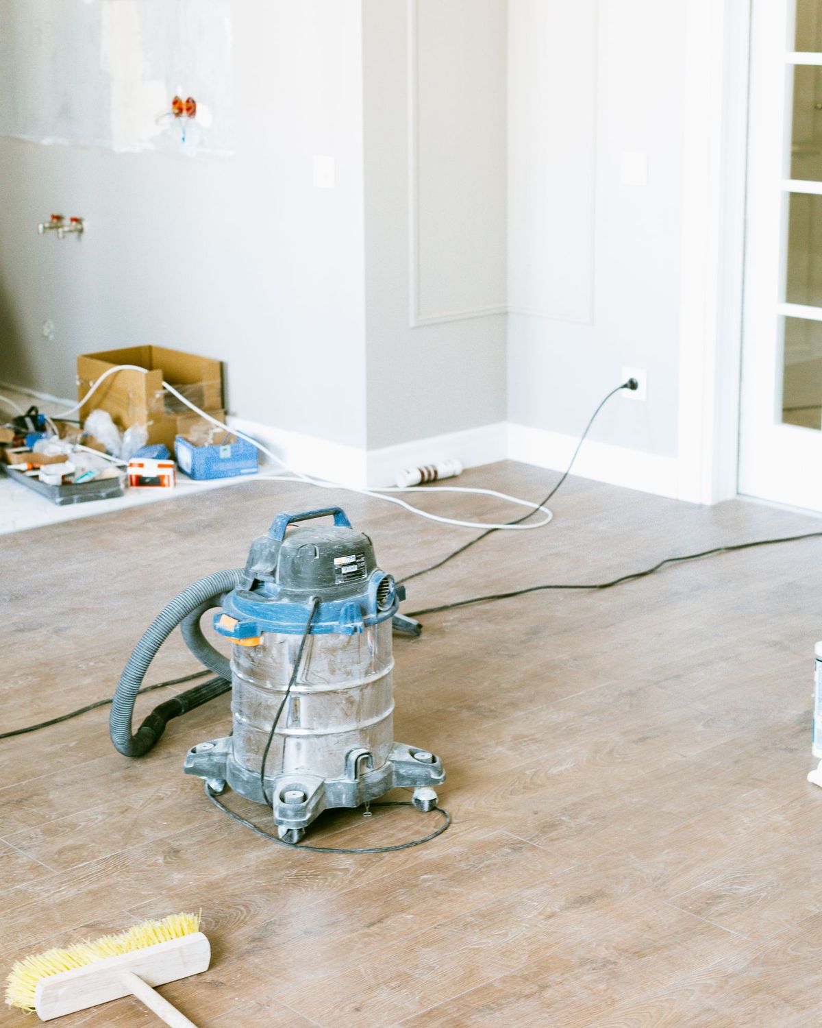 Shop vacuum and push broom in a freshly renovated room with construction dust on the floor (stock photo)